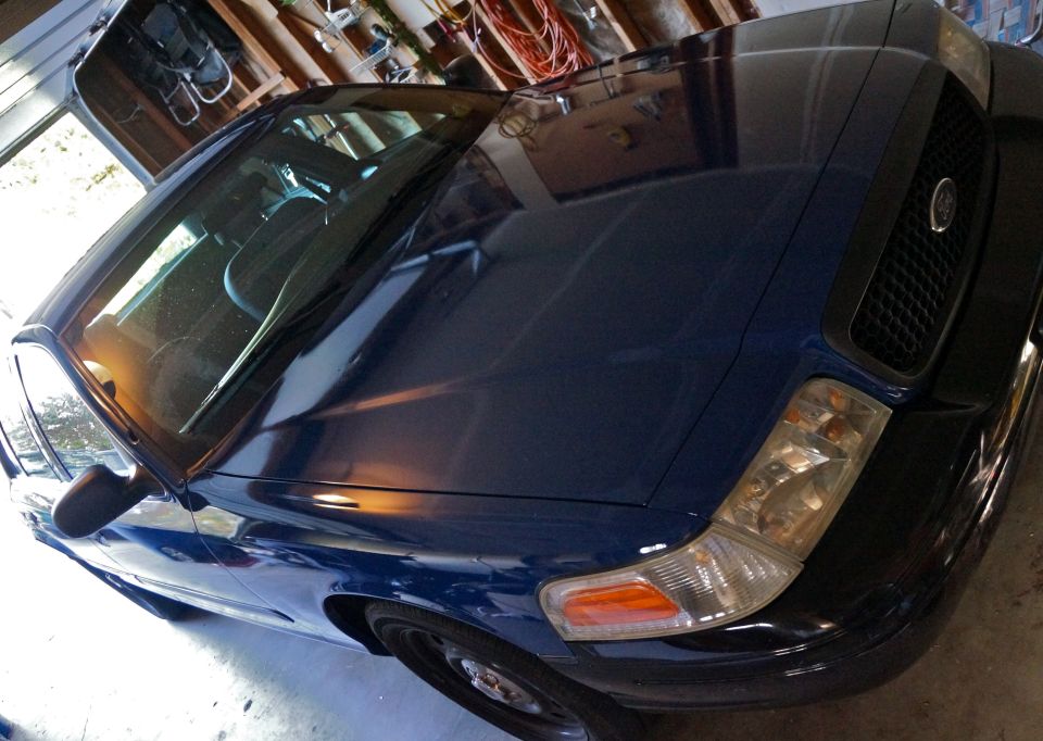 Dark blue sedan, front quarter view, parked indoors. Headlights and grille are visible