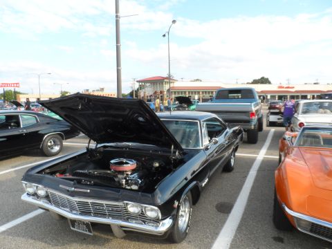 1971 Ford Ranchero - A black 1965 Chevrolet Impala coupe is displayed with its hood open, revealing the engine, at an outdoor car show.