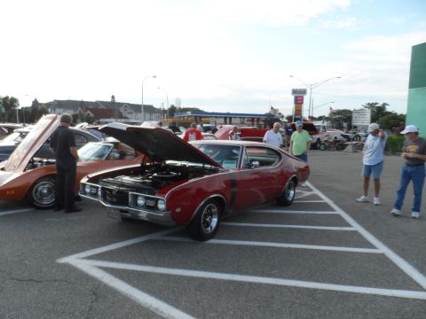 1971 Ford Ranchero - Several cars are parked at an outdoor event, with one red muscle car's hood open.