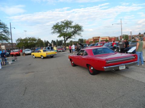 1971 Ford Ranchero - Red 1969 Plymouth Road Runner and yellow classic car at an outdoor event with other vehicles and people.