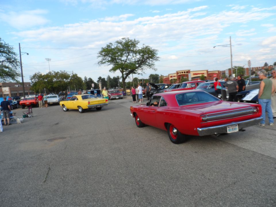 Red 1969 Plymouth Road Runner seen from rear, parked next to yellow classic car at outdoor car show