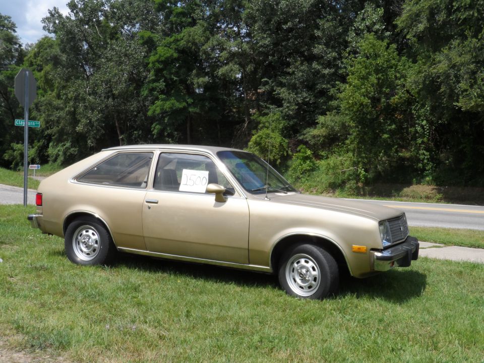 Gold hatchback car parked on grass, side view. Price tag in window