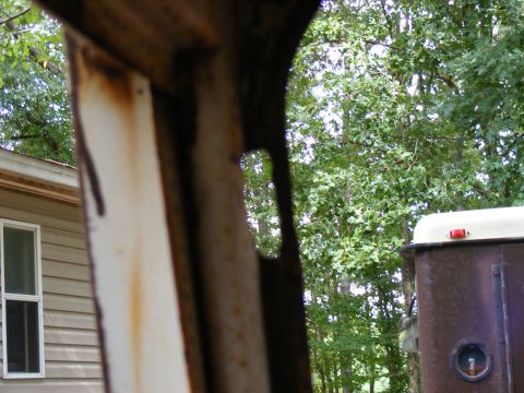 1978 Ford Bronco - View through rusty metal framing shows trees and a house; Supermotors.net logo is present.