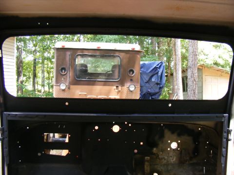 1978 Ford Bronco - The rear of a vintage pickup truck is visible through an open window, with trees and a building in the background.
