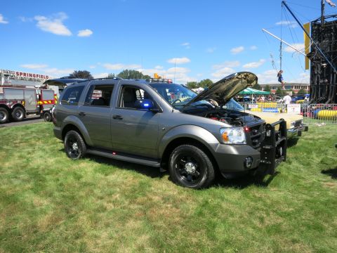 2001 Ford Crown Victoria - Gray Dodge Durango SUV with police lights and push bumper, hood open, parked on grass at an outdoor event.
