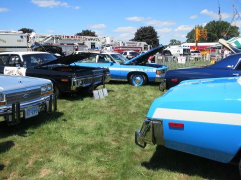 2001 Ford Crown Victoria - Multiple vintage police cars are displayed on a grassy field under a partly cloudy sky.
