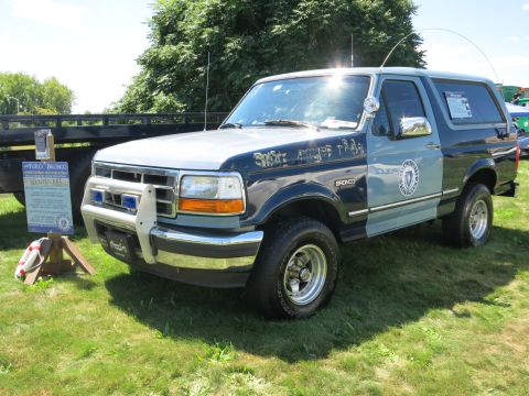 2001 Ford Crown Victoria - A Ford Bronco, likely from the 1990s, is parked on a grassy field with a sign next to it.