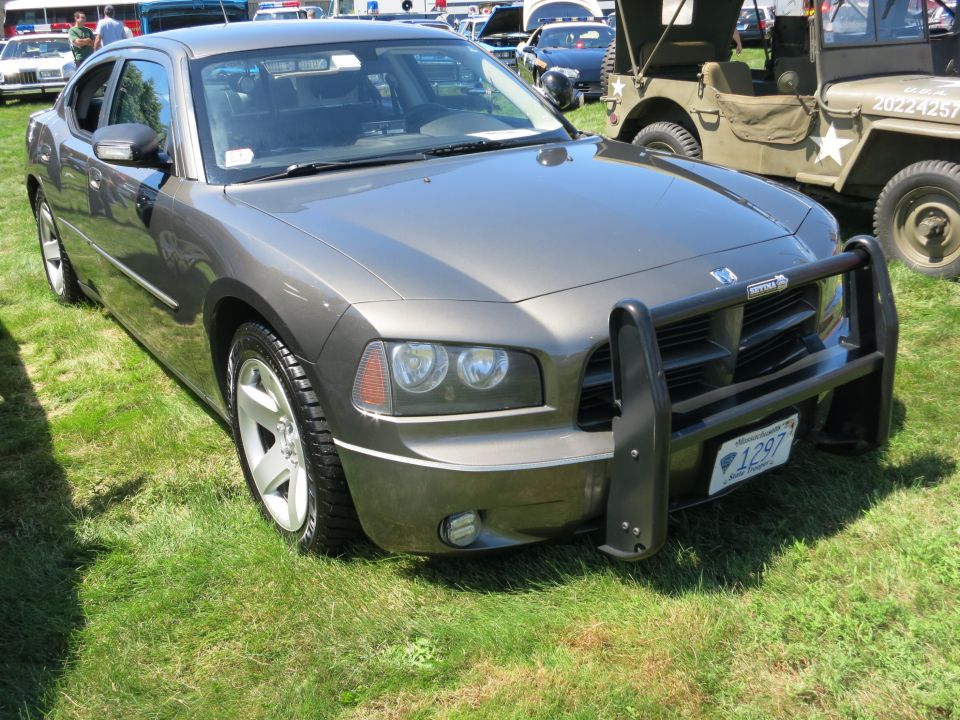 Gray Dodge Charger police car with push bar parked on grass, other vehicles in background