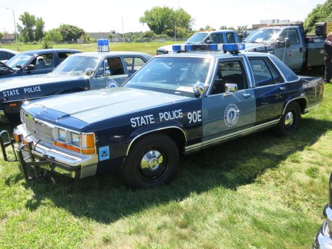 2001 Ford Crown Victoria - A police car with "STATE POLICE 90E" markings is parked on grass next to other vehicles.