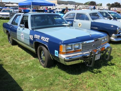 2001 Ford Crown Victoria - A vintage police car, likely from the 1980s, is displayed outdoors with other vehicles.