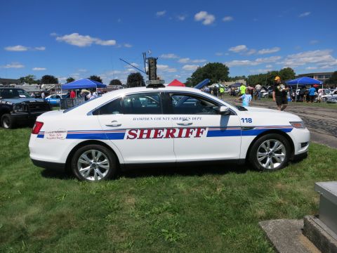 2001 Ford Crown Victoria - A white sheriff's department sedan is parked on grass at an outdoor event with other vehicles and people visible.