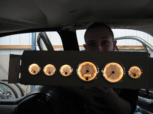 Illuminated aftermarket six-gauge cluster with cream faces held up inside a car