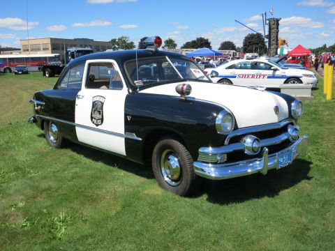 2001 Ford Crown Victoria - This vintage police car, likely from the early 1950s, is displayed outdoors with other vehicles and tents in the background.