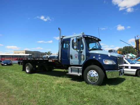 2001 Ford Crown Victoria - A two-tone blue and gray tow truck is parked on a grassy field under a blue sky with scattered clouds.