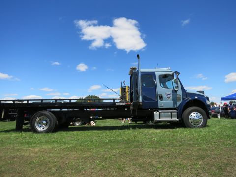 2001 Ford Crown Victoria - A tow truck with a flatbed is parked on a grassy field on a sunny day.