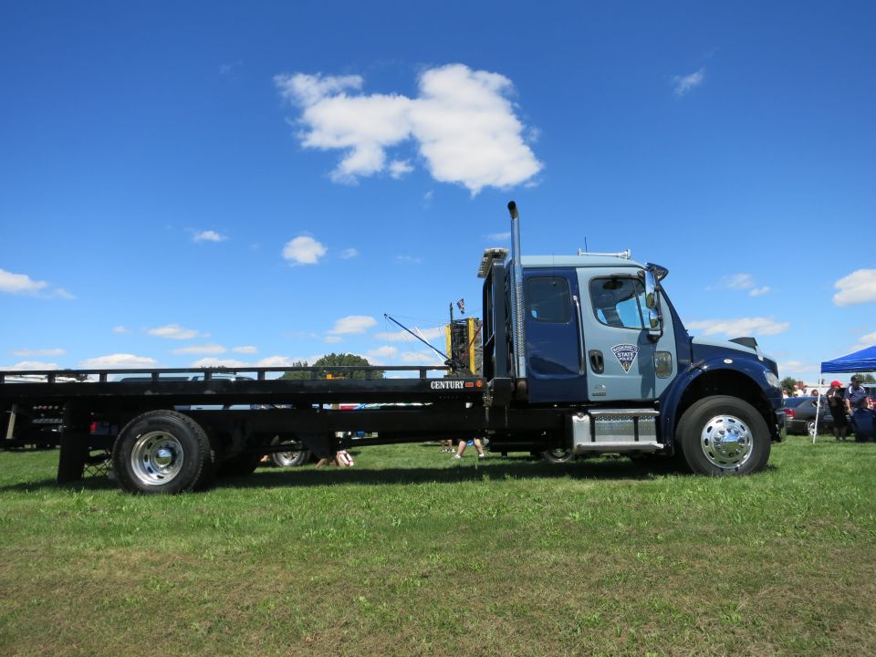 tow truck with flatbed, blue and gray cab, parked on grass under blue sky