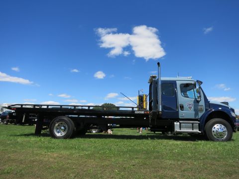 2001 Ford Crown Victoria - A tow truck with a flatbed is parked on a grassy field on a sunny day.