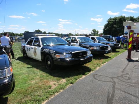 2001 Ford Crown Victoria - Several police cars are lined up on a sunny day, with some people standing nearby.