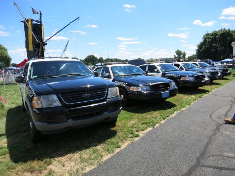 2001 Ford Crown Victoria - Several police vehicles, including Ford Crown Victorias, are parked on a grassy area next to a road.