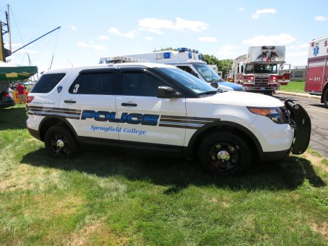 2001 Ford Crown Victoria - A police SUV marked "POLICE Springfield College" is parked on grass, with an ambulance and fire truck in the background.