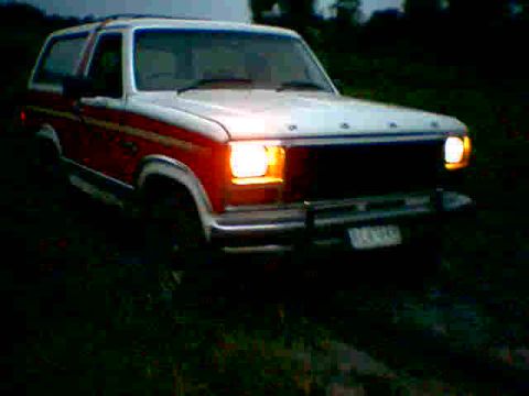 1981 Ford Bronco - A white and red Ford Bronco is visible in a dimly lit outdoor setting, with its front lights illuminated.