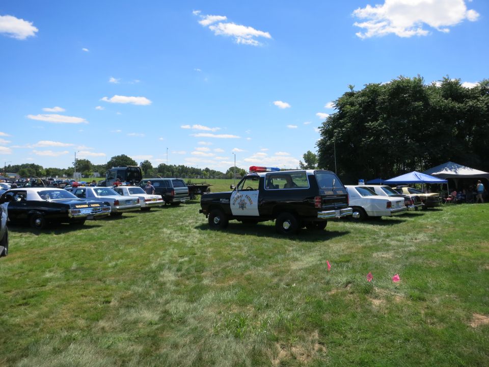 Police SUV and sedans parked on grass under a blue sky