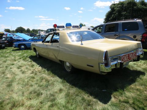 2001 Ford Crown Victoria - A vintage tan police car is displayed outdoors with other vehicles under a sunny sky.