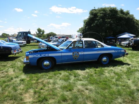 2001 Ford Crown Victoria - A vintage police car with its hood open is parked on a grassy field alongside other vehicles.