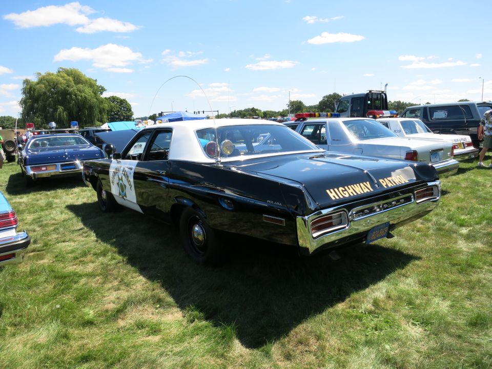 Black and white highway patrol car, text on rear says "HIGHWAY PATROL". Other cars parked nearby