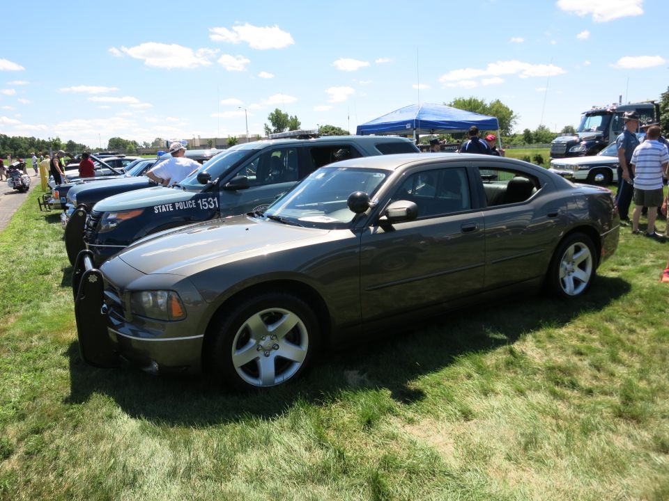 Dark gray Dodge Charger police car, front passenger side view, parked on grass