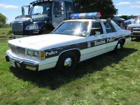 2001 Ford Crown Victoria - A Boston Police car with a light bar is parked next to a State Police truck.