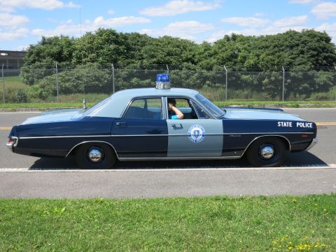 2001 Ford Crown Victoria - A vintage police car, painted in a two-tone blue and gray scheme, is seen driving on a road.