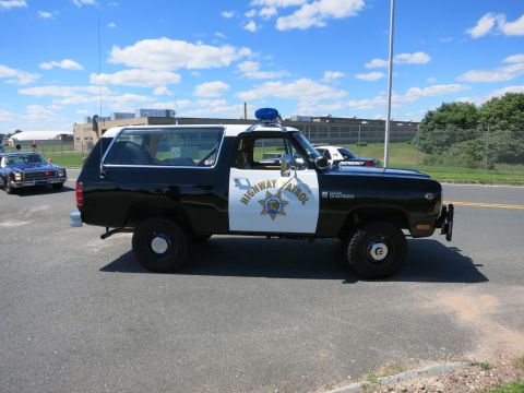 2001 Ford Crown Victoria - A Dodge Ramcharger SUV, likely from the early 1980s, is parked on the side of the road with a police livery.