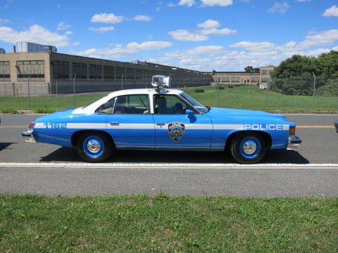 2001 Ford Crown Victoria - Side view of a vintage blue and white police sedan parked on a street.
