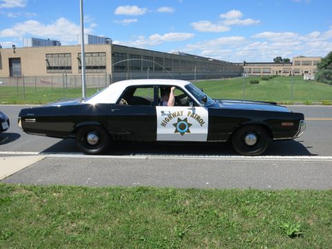 2001 Ford Crown Victoria - A classic black and white patrol car with a white roof is seen driving on a sunny day.