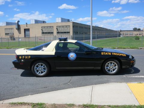 2001 Ford Crown Victoria - Side view of a black and tan police car, identified as a 1993 Chevrolet Camaro, with state trooper markings.