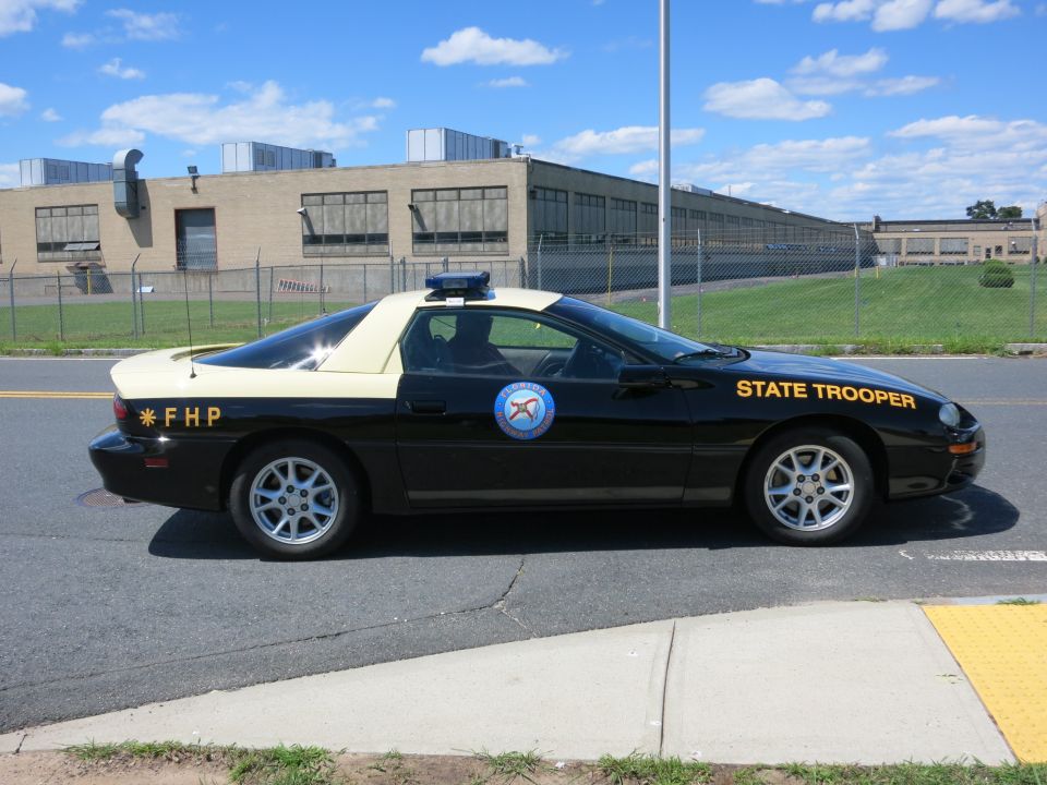 Black and tan police car with "STATE TROOPER" on door and "*FHP" on fender. Appears to be a 1993 Chevrolet Camaro