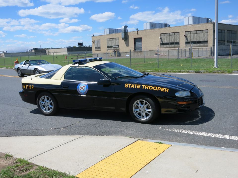 State trooper car with 'STATE TROOPER' text on door, parked near a silver Corvette