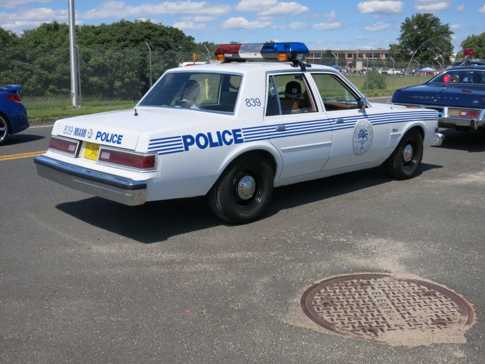 White police car with blue stripes and "POLICE" text, parked on asphalt