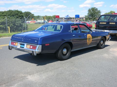 2001 Ford Crown Victoria - A blue police car with a badge on the door is parked next to a black vehicle with 'HIGHWAY PATROL' text.