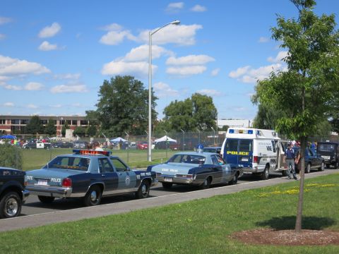 2001 Ford Crown Victoria - Line of vintage police sedans and a van parked on a sunny day.