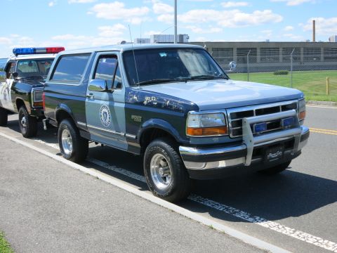 2001 Ford Crown Victoria - Two police vehicles, a Ford Bronco and another SUV, are parked on the side of the road.