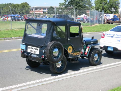 2001 Ford Crown Victoria - Vintage Jeep CJ-3A police vehicle with 'LOOK PARK POLICE' text on the back.