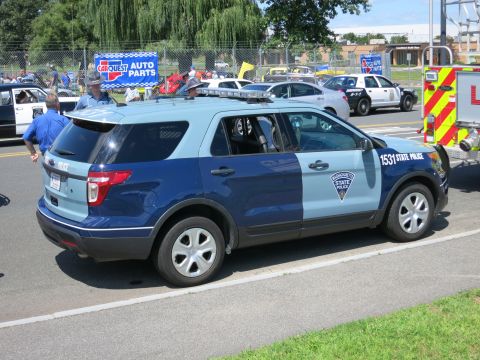 2001 Ford Crown Victoria - A two-tone police SUV is parked on the side of the road with other vehicles and people in the background.