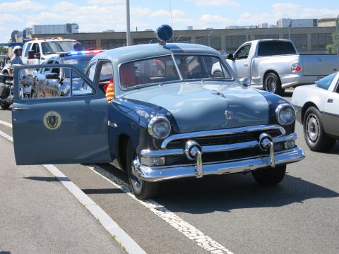 2001 Ford Crown Victoria - A vintage police car with its door open sits parked next to other vehicles.