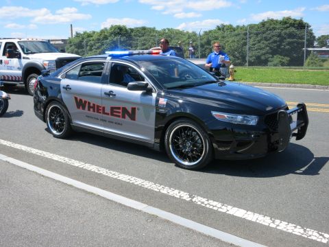 2001 Ford Crown Victoria - A police car with Whelen branding and a light bar is parked on the street, with another vehicle and two officers visible.