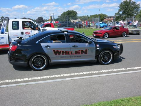 2001 Ford Crown Victoria - A Whelen police car is parked on the street with other vehicles and a tow truck nearby.