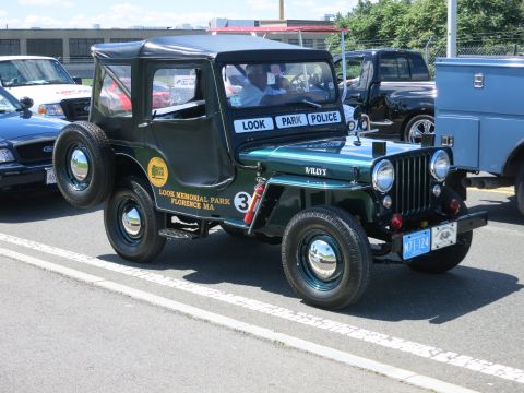 2001 Ford Crown Victoria - A green Willys Jeep, marked as 'LOOK PARK POLICE', is parked next to other vehicles.