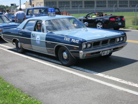 2001 Ford Crown Victoria - A classic state police car with a light bar on top is parked on the side of the road.