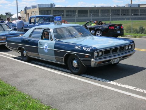 2001 Ford Crown Victoria - A vintage police car with a light bar on top is parked next to other vehicles on a sunny day.
